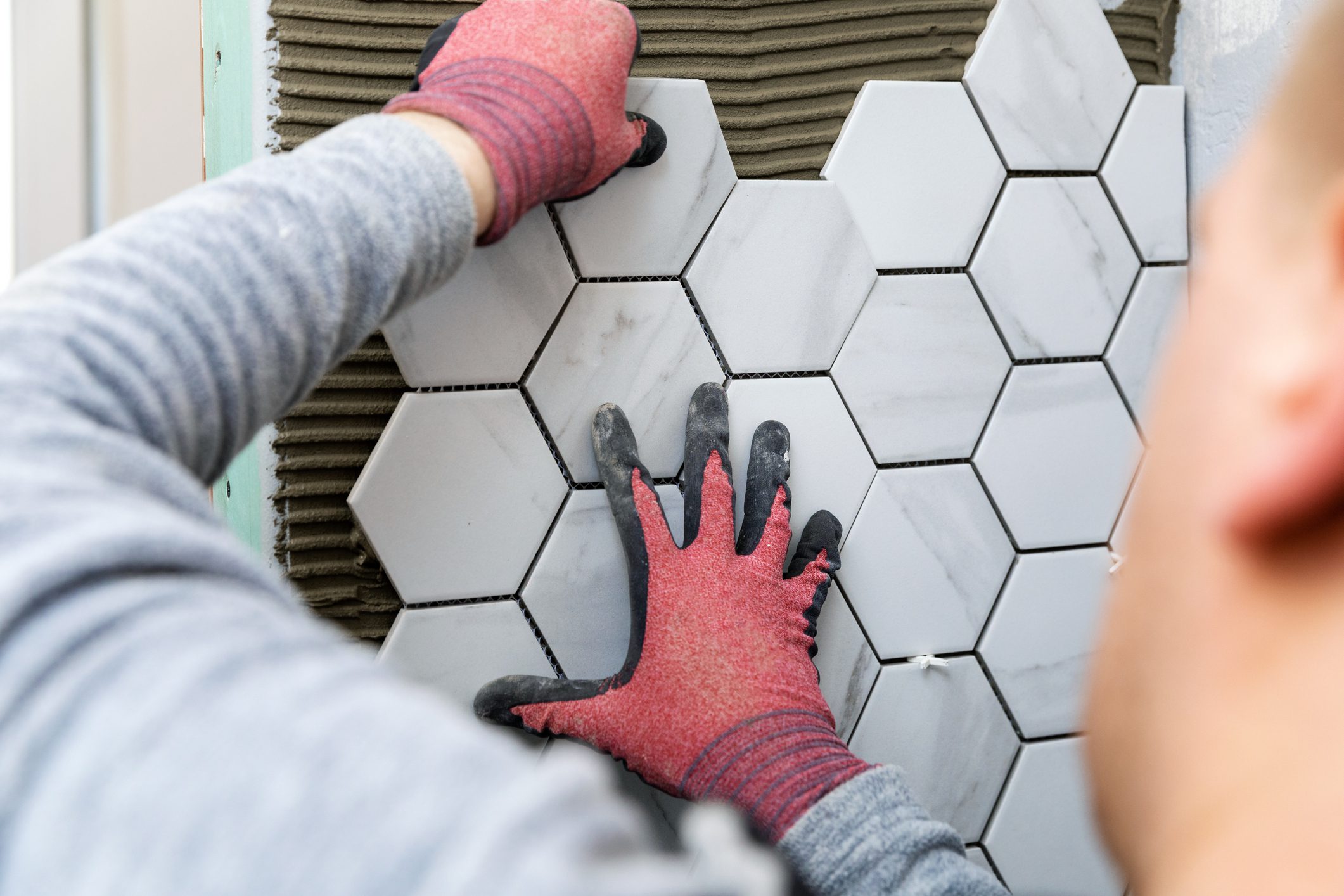 Person installing hexagonal tiles on wall.