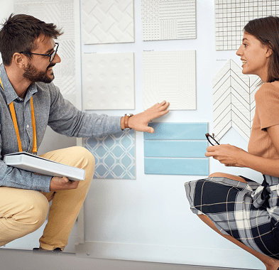 Two people discussing tile samples on wall.